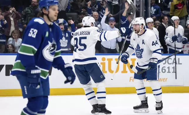 Toronto Maple Leafs' Morgan Rielly (44) celebrates after his goal with teammate Oliver Ekman-Larsson (95) as Vancouver Canucks' Teddy Blueger (53) skates past during the second period of an NHL hockey game in Vancouver, British Columbia, Saturday, Feb. 8, 2025. (Ethan Cairns/The Canadian Press via AP)