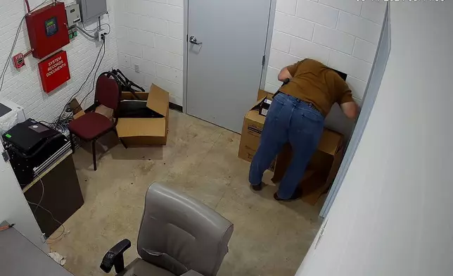 This image from a security camera footage provided by the Cullman County Sheriff's Office shows an individual who works at there sticks his head and upper body in the hole, attempting to open the door to the evidence room, at the Hanceville Police Department in Hanceville, Ala. Officials said the evidence room was not kept secure and could be accessed by a hole on the wall. (Cullman County Sheriff's Office via AP)