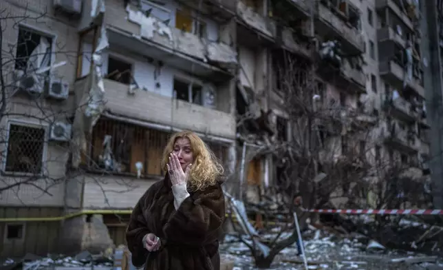 FILE - Natali Sevriukova reacts next to her house following a rocket attack the city of Kyiv, Ukraine, on Feb. 25, 2022. The yearlong war in Ukraine has left tens of thousands of dead and wounded on both sides, disrupted energy and food supplies, and reduced whole cities to ruins. (AP Photo/Emilio Morenatti, File)
