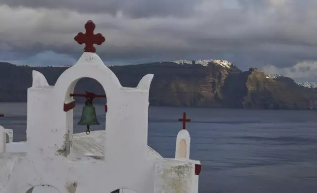 A bell towel of an Orthodox church in the town of Oia on the earthquake-struck island of Santorini, Greece, as the main town of Fira is litted by the sun in the background on Tuesday, Feb. 4, 2025. (AP Photo/Petros Giannakouris)