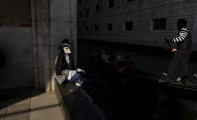 A reveller participating in the celebrations of the historic Venetian Carnival rests as a gondola passes by, in Venice, Italy, Saturday, Feb. 15, 2025. (AP Photo/Antonio Calanni)