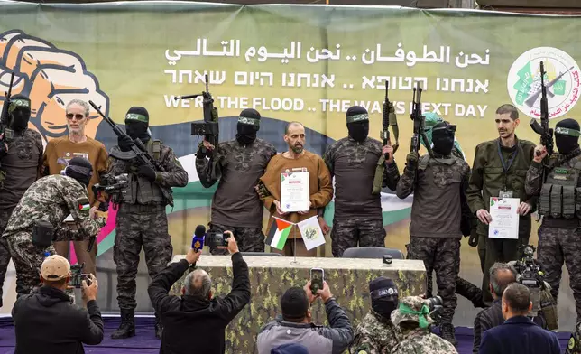 Israeli captives, from left to the right, Ohad Ben Ami, Eli Sharabi and Or Levy, who have been held hostage by Hamas in Gaza since Oct. 7, 2023, are escorted by Hamas fighters on a stage before being handed over to the Red Cross in Deir al-Balah, central Gaza Strip, Saturday, Feb. 8, 2025. (AP Photo/Abdel Kareem Hana)