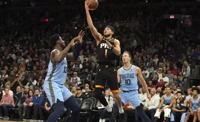 Phoenix Suns guard Devin Booker (1) drives between Memphis Grizzlies guard Ja Morant and guard Luke Kennard (10) during the first half of an NBA basketball game, Tuesday, Feb. 11, 2025, in Phoenix. (AP Photo/Rick Scuteri)