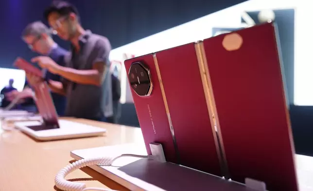 Visitors look at a display during the sales global opening of Huawei's industry's first tri-foldable phone, right, in Kuala Lumpur, Malaysia, Tuesday, Feb. 18, 2025. (AP Photo/Vincent Thian)