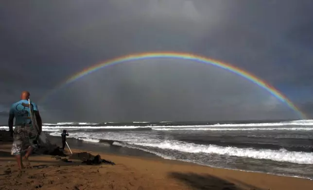 FILE - Professional surfers make their way to the water while a large rainbow crosses the ocean during the Pro Hawaii surfing contest at Ali'i Beach in Haleiwa, Hawaii, Nov. 18, 2005. (AP Photo/Lucy Pemoni, File)