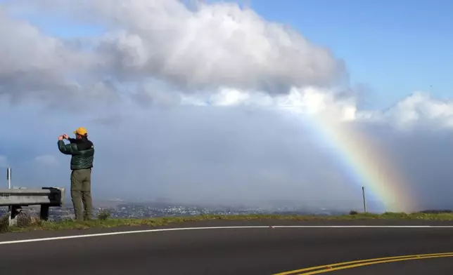 FILE - A tourist takes photos of a rainbow on the road that leads to Haleakala National Park on the Hawaiian island of Maui, Dec. 19, 2012. (AP Photo/Martha Irvine, File)