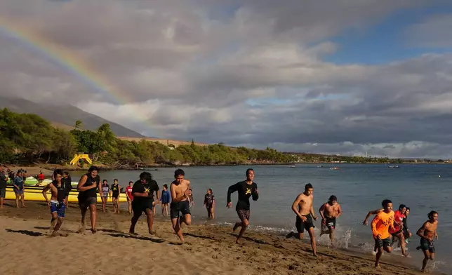 Members of the Napili Canoe Club run on the beach as a rainbow forms nearby on Monday, July 8, 2024, at Hanakao'o Park in Lahaina, Hawaii. (AP Photo/Lindsey Wasson)