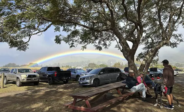 People gather outside a farmers market while a rainbow appears in the background in Kamuela, Hawaii, on Dec. 11, 2024. (AP Photo/ Audrey McAvoy)
