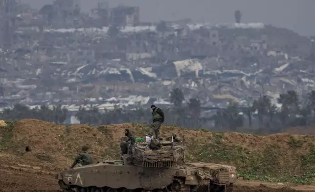Destroyed buildings by Israeli bombardments inside the northern Gaza Strip can be seen as Israeli soldiers work on their tank in southern Israel, Tuesday, Feb.11, 2025. (AP Photo/Ariel Schalit)