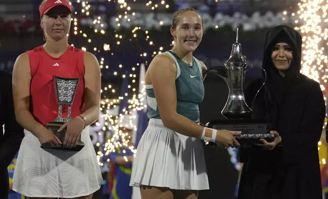 The runner-up, Denmark's Clara Tauson, left, stands while Russia's Mirra Andreeva is presented the winner's trophy by Sheikha Latifa after the Dubai Duty-Free Tennis Championship final match in Dubai, United Arab Emirates, on Saturday, Feb. 22, 2025. (AP Photo/Altaf Qadri)