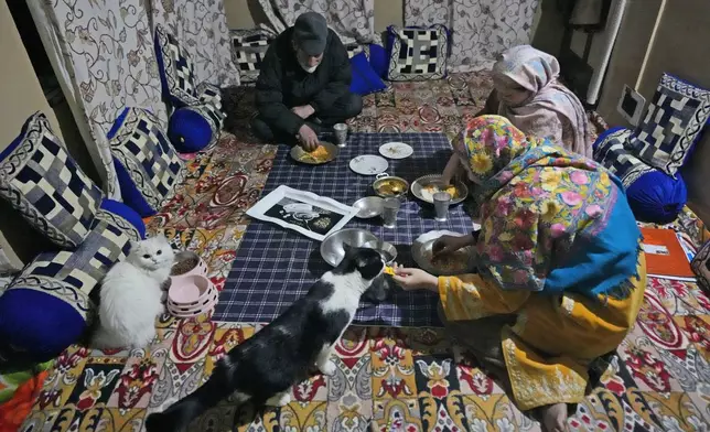 A Kashmiri family eats dinner with their pet cats sitting beside them inside in Srinagar, Indian controlled Kashmir, Wednesday, Feb. 12, 2025 (AP Photo/Mukhtar Khan)