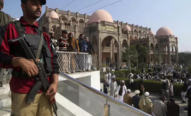 A police officer stands guard as mourners arrive to attend the funeral prayer of a senior Muslim cleric, Hamidul Haq who was killed in the Friday's suicide bomb attack, at a pro-Taliban seminary in Akora Khattak, Pakistan, Saturday, March 1, 2025. (AP Photo/Muhammad Sajjad)