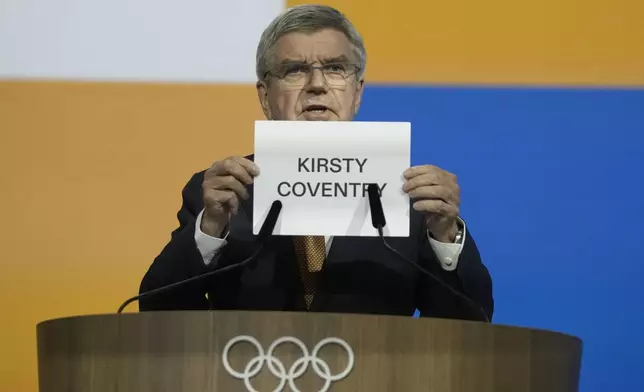 IOC President Thomas Bach holds up the name of Kirsty Coventry as she is announced as the new IOC President at the International Olympic Committee 144th session in Costa Navarino, western Greece, Thursday, March 20, 2025. (AP Photo/Thanassis Stavrakis)