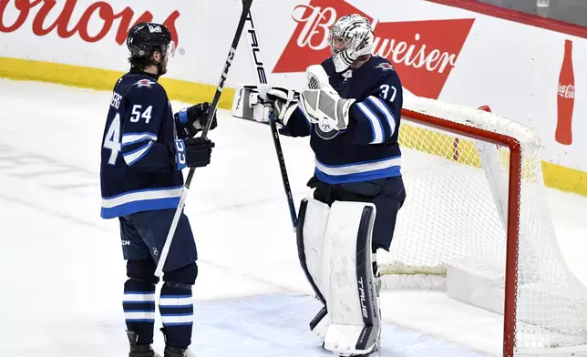 Winnipeg Jets goaltender Connor Hellebuyck (37) celebrates the win over the New York Rangers with Dylan Samberg (54) following the third period of an NHL hockey game in Winnipeg, Manitoba, Tuesday, March 11, 2025. (Fred Greenslade/The Canadian Press via AP)