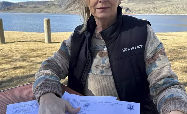 Former Grand Coulee Dam worker, Stephanie Duclos, sits at a picnic table in front of Banks Lake in Electric City, Wash., holding a letter from the Department of Interior, Bureau of Reclamation on Friday, Feb. 28, 2025, saying she has been terminated from her job. (AP Photo/Martha Bellisle)