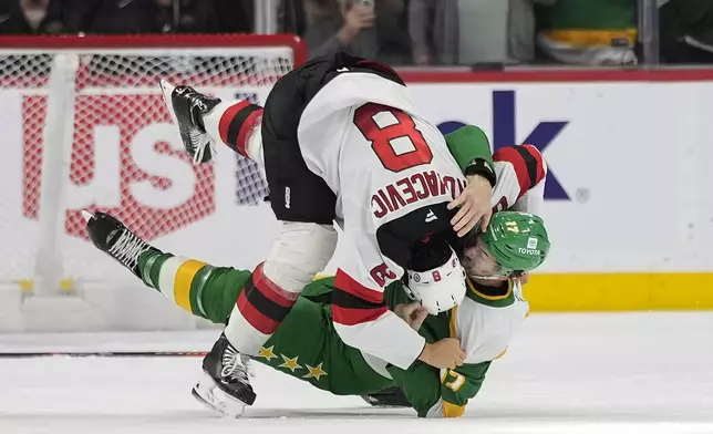 New Jersey Devils defenseman Johnathan Kovacevic (8) and Minnesota Wild left wing Marcus Foligno (17) fight during the second period of an NHL hockey game, Saturday, March 29, 2025, in St. Paul, Minn. (AP Photo/Abbie Parr)