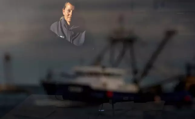 Meghan Lapp, who works for the fishing company Seafreeze Limited, is reflected in a photograph of a fishing vessel at the company's plant Wednesday, Jan. 15, 2025, in Narragansett, R.I. "We created the Clean Water Act so we wouldn't be dumping chemicals into the ocean," said Lapp who has joined some fellow fishermen pointing to the unknown impacts of a carbon capture experiment on one of the most productive fishing grounds on the eastern seaboard. "What are we thinking?" (AP Photo/David Goldman)