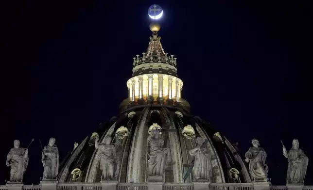 The moon moves behind the cross on top of St Peter's Basilica ahead of the recitation of the Holy Rosary for Pope Francis' health in St Peter's Square at the Vatican, Monday, March 3, 2025. (AP Photo/Kirsty Wigglesworth)