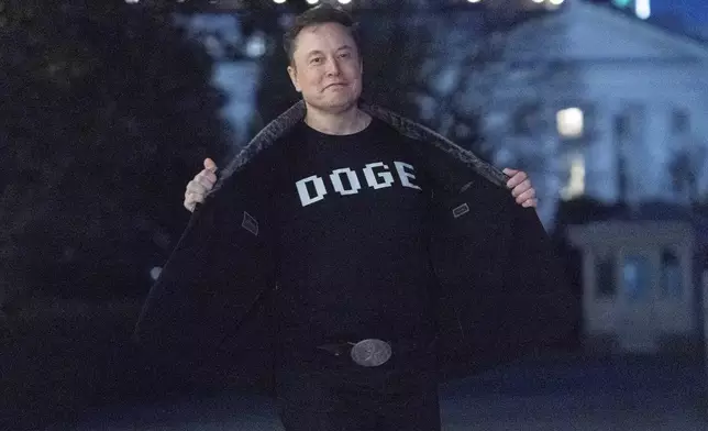 Elon Musk flashes his t-shirt that reads "DOGE" to the media as he walks on South Lawn of the White House, in Washington, Sunday, March 9, 2025. (AP Photo/Jose Luis Magana)