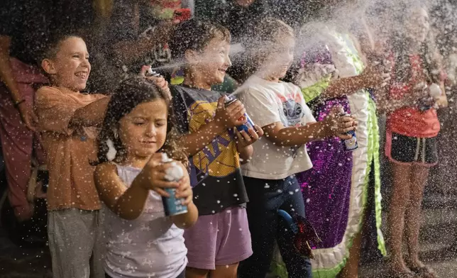 Children spray foam at performers during a Carnival parade in Montevideo, Uruguay, Wednesday, Feb. 19, 2025. (AP Photo/Matilde Campodonico)