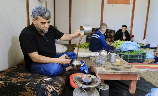 A man serves tea as volunteers prepare Bazin, a traditional Libyan dough bread made of barley or whole wheat flour and often served with stew in Tajoura, east of Libya's capital Tripoli, Tuesday, March 11, 2025, during the Muslim holy month of Ramadan. (AP Photo/Yousef Murad)