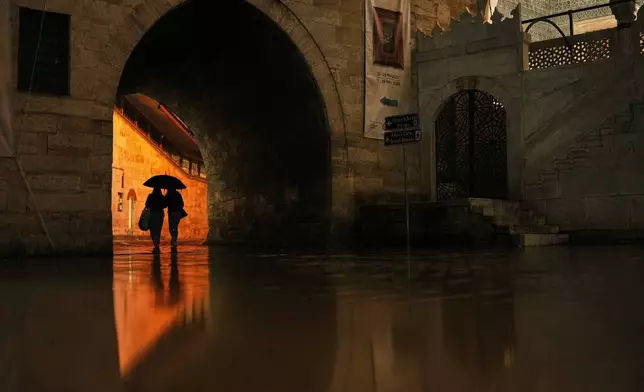 Passersby shelter against the rain with an umbrella next to Yeni Camii or New Mosque, in Istanbul, Turkey, Friday, March 28, 2025. (AP Photo/Francisco Seco)