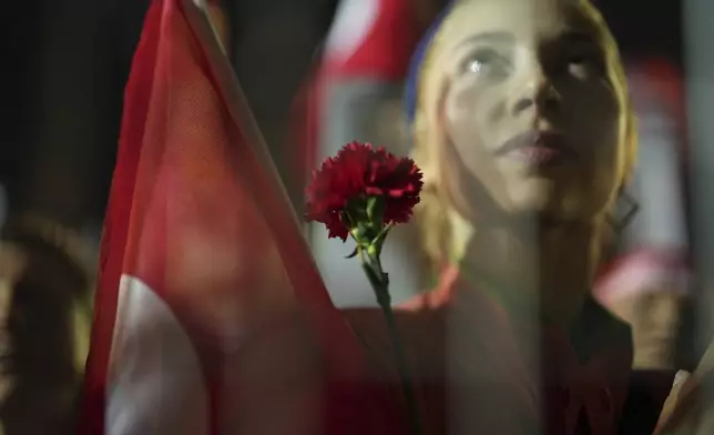 A protesters holds a flower as stand behind police barrier during a protest after Istanbul's Mayor Ekrem Imamoglu was arrested and sent to prison, in Istanbul, Turkey, Tuesday, March 25, 2025. (AP Photo/Francisco Seco)