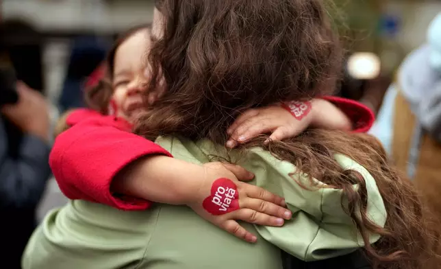 A child with heart shaped stickers on her hands, reading "Pro-Life" hugs a woman during an anti-abortion march in Bucharest, Romania, Saturday, March 29, 2025. (AP Photo/Vadim Ghirda)