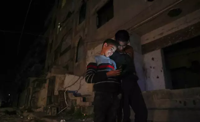 Two boys look at a cellphone in a dark street in Damascus, Syria, early Thursday March 27, 2025. Neighborhoods in most parts of the country turn pitch black once the sunsets, save on some lights from street lamps, Mosque minarets, and drivers with their floodlights on to see.(AP Photo/Omar Sanadiki)