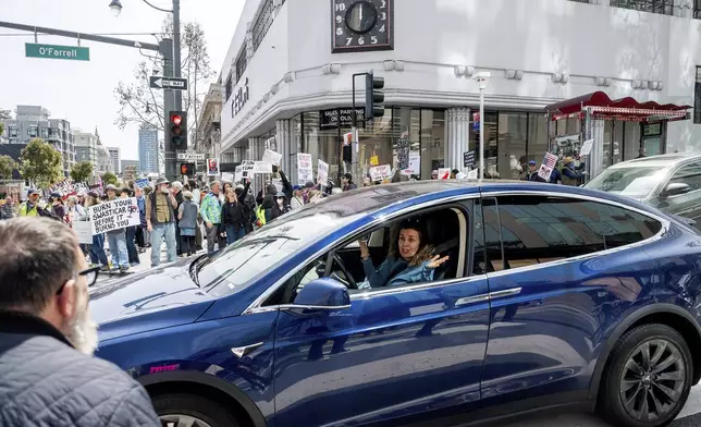 A Tesla driver shrugs while passing protesters against Tesla CEO Elon Musk in San Francisco on Saturday, March 29, 2025. (AP Photo/Noah Berger)