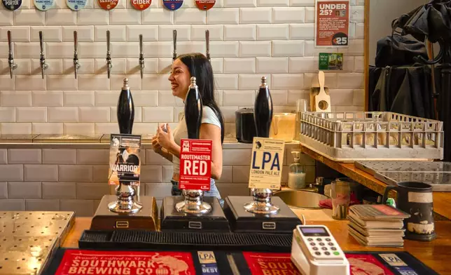 A staff member laughs during her shift in the Southwark Brewing Co., one of the bars on the Bermondsey Beer Mile in south London, Saturday March 8, 2025. (AP Photo/Tony Hicks)