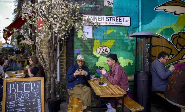 Customers sit outside the Beer Bar on the Bermondsey Beer Mile in south London, Saturday March 8, 2025. (AP Photo/Tony Hicks)