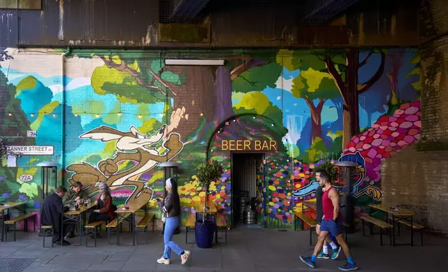 People walk past the Beer Bar on the Bermondsey Beer Mile in south London, Saturday March 8, 2025. (AP Photo/Tony Hicks)