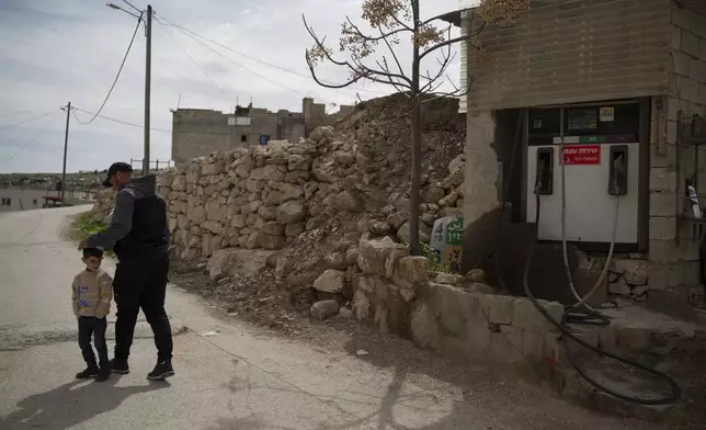 Salem Adra, walks with his 4-year-old son Elias, past his family's gas station, featured in the Oscar-winning documentary "No Other Land," co-directed by his brother Palestinian activist Basel Adra, at the West Bank village of Tuwani, Monday, March 3, 2025. (AP Photo/Leo Correa)