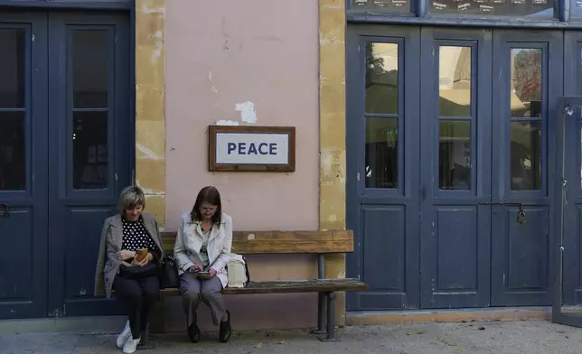 Women sit on a bench next to a checkpoint crossing point at Ledra street in divided capital Nicosia, Cyprus, Tuesday, March 18, 2025. (AP Photo/Petros Karadjias)