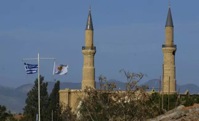 A Cyprus' and a Greek flags, are seen on the pols in the south, as in the background are seen the minarets of the Selimiye mosque, or Cathedral of St Sophia, or Agia Sofia, in the Turkish occupied area in the north, in divided capital Nicosia, Cyprus, Tuesday, March 18, 2025. (AP Photo/Petros Karadjias)