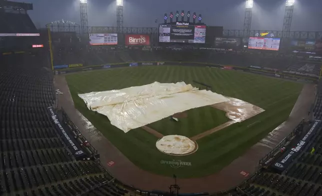 The grounds crew covers the field with a tarp during a rain delay in the seventh inning of a baseball game between the Los Angeles Angels and the Chicago White Sox in Chicago, Sunday, March 30, 2025. (AP Photo/Nam Y. Huh)