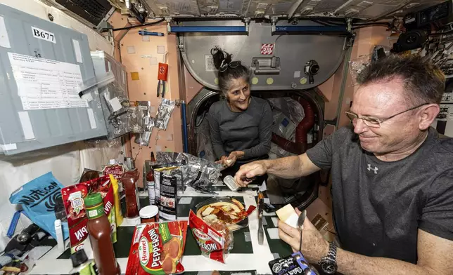 FILE - In this photo released by NASA, astronauts Suni Williams and Butch Wilmore, both Expedition 71 Flight Engineers, make pizza aboard the International Space Station's galley located inside the Unity module on Sept. 9, 2024. Items are attached to the galley using tape and velcro to keep them from flying away in the microgravity environment. (NASA via AP, File)