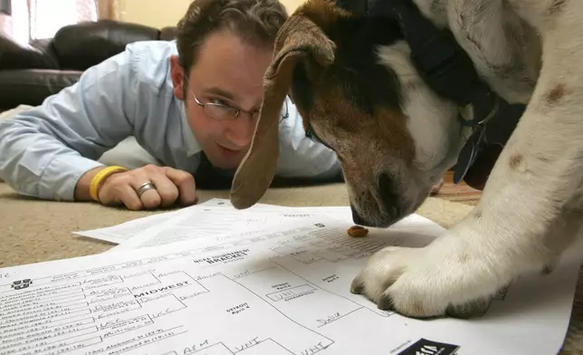 FILE - Bryan Zygmont works with his dog, Romey, to fill out the 2009 NCAA Tournament brackets at his Dubuque, Iowa, home Tuesday, March 17, 2009. (Jeremy Portje/Telegraph Herald via AP, File)