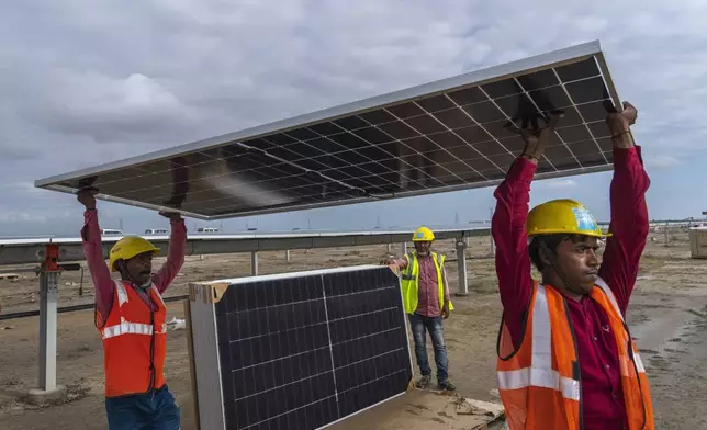 FILE - Workers carry a solar panel for installation at the under-construction Adani Green Energy Limited's Renewable Energy Park in the salt desert of Karim Shahi village, near Khavda, Bhuj district near the border with Pakistan, in the western state of Gujarat, India, on Sept. 21, 2023. (AP Photo/Rafiq Maqbool, File)