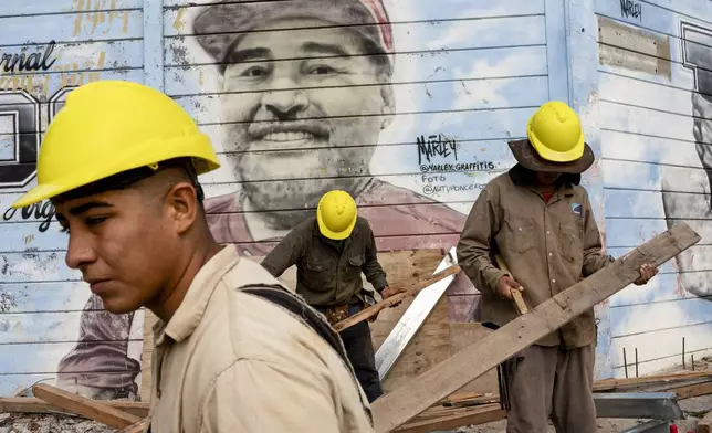 Construction workers stand by a mural of late soccer star Diego Maradona at the stadium of the Argentinos Juniors soccer club, Maradona's first pro team, in Buenos Aires, Argentina, Tuesday, March 11, 2025, the day members of the medical team that treated Maradona before his death go on trial for homicide by negligence. (AP Photo/Rodrigo Abd)