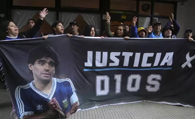 Fans of the late soccer star Diego Maradona hold a banner that reads in Spanish "Justice for God" outside the court where members of the medical team that treated Maradona go on trial for alleged homicide by negligence in San Isidro on the outskirts of Buenos Aires, Argentina, Tuesday, March 11, 2025. (AP Photo/Natacha Pisarenko)