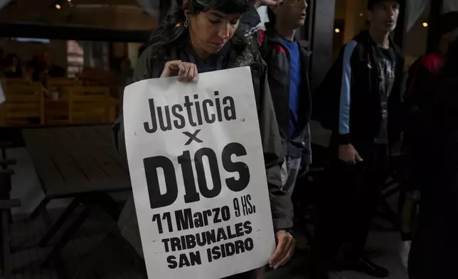 A fan of the late soccer star Diego Maradona holds a sign that reads in Spanish "Justice for God" outside the court where members of the medical team that treated Maradona go on trial for alleged homicide by negligence in San Isidro on the outskirts of Buenos Aires, Argentina, Tuesday, March 11, 2025. (AP Photo/Natacha Pisarenko)