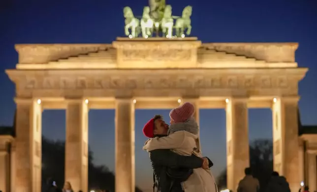 A couple hugs in front of the Brandenburg Gate in Berlin, Germany, Tuesday, March 18, 2025. (AP Photo/Ebrahim Noroozi)