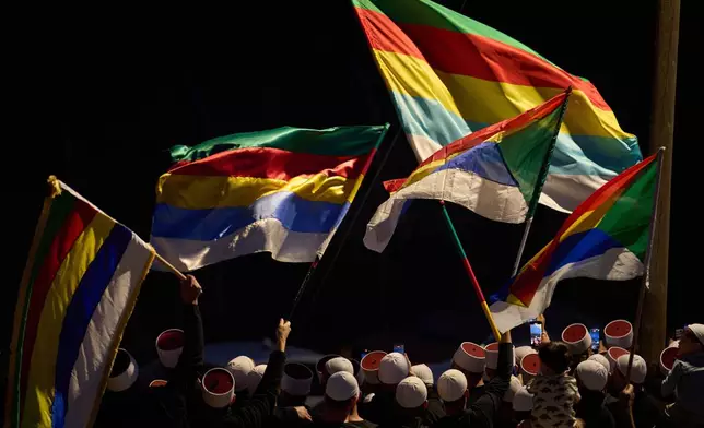 Members of the Druze community of the town of Majdal Shams, wave flags to say goodbye to Syrian Druze clerics, before they cross the border back to Syria, as seen from the Israeli-annexed Golan Heights, Saturday, March 15, 2025. (AP Photo/Leo Correa)