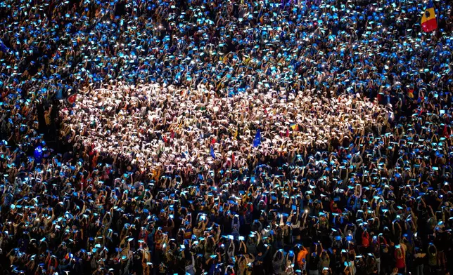 People shine lights behind coloured papers attempting to make a heart shape during a pro-European rally, joined by thousands, to counter what the organizers described as a "wave of sovereignism and ultranationalism", outside the government headquarters in Bucharest, Romania, Saturday, March 15, 2025. (AP Photo/Andreea Alexandru)