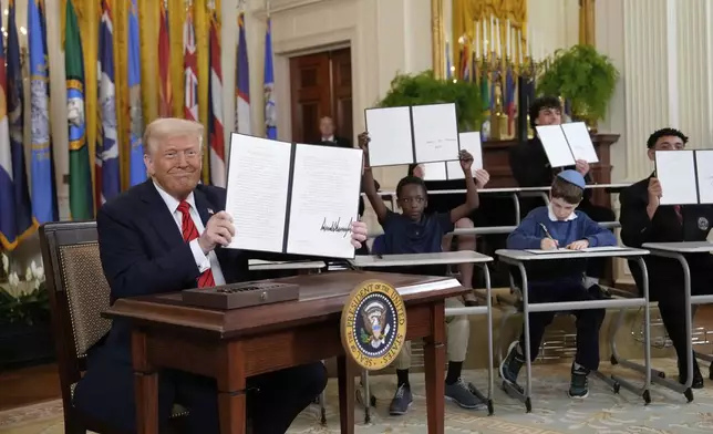 President Donald Trump, left, holds up a signed executive order as young people hold up copies of the executive order they signed at an education event in the East Room of the White House in Washington, Thursday, March 20, 2025. (AP Photo/Ben Curtis)
