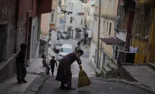 A girl sweeps the street outside her family's home as other children play in a poor neighborhood in Istanbul, Turkey, Saturday, March 15, 2025. (AP Photo/Khalil Hamra)