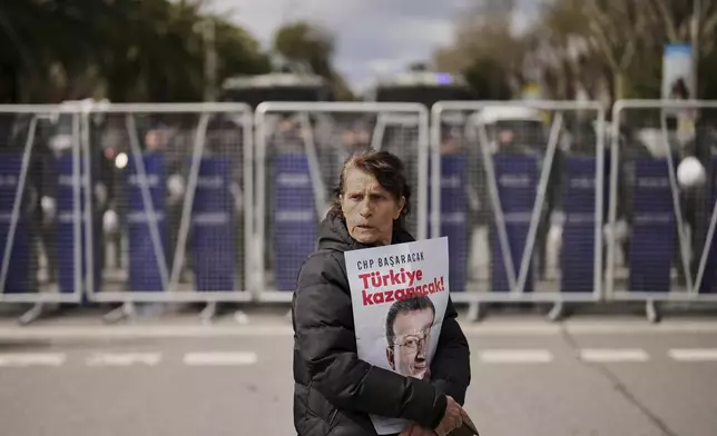 A woman protests, holding a poster of Istanbul Mayor Ekrem Imamoglu, in front of a police cordon blocking the roads leading to the Vatan Security Department, where Imamoglu is expected to be taken following his arrest in Istanbul, Turkey, Wednesday, March 19, 2025. (AP Photo/Francisco Seco)