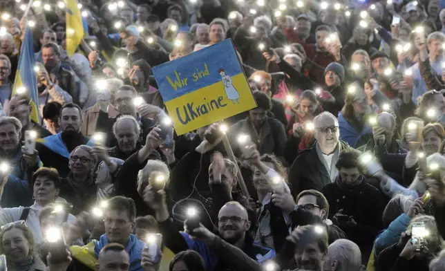 People hold up cell phone lights as they take part in a demonstration against Russia's war on Ukraine, in Berlin, Germany, Sunday, March 9, 2025. (AP Photo/Markus Schreiber)